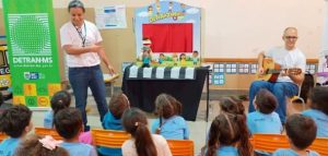 imagem detran vai a escola: dois adultos estão apresentado para uma turma de crianças.